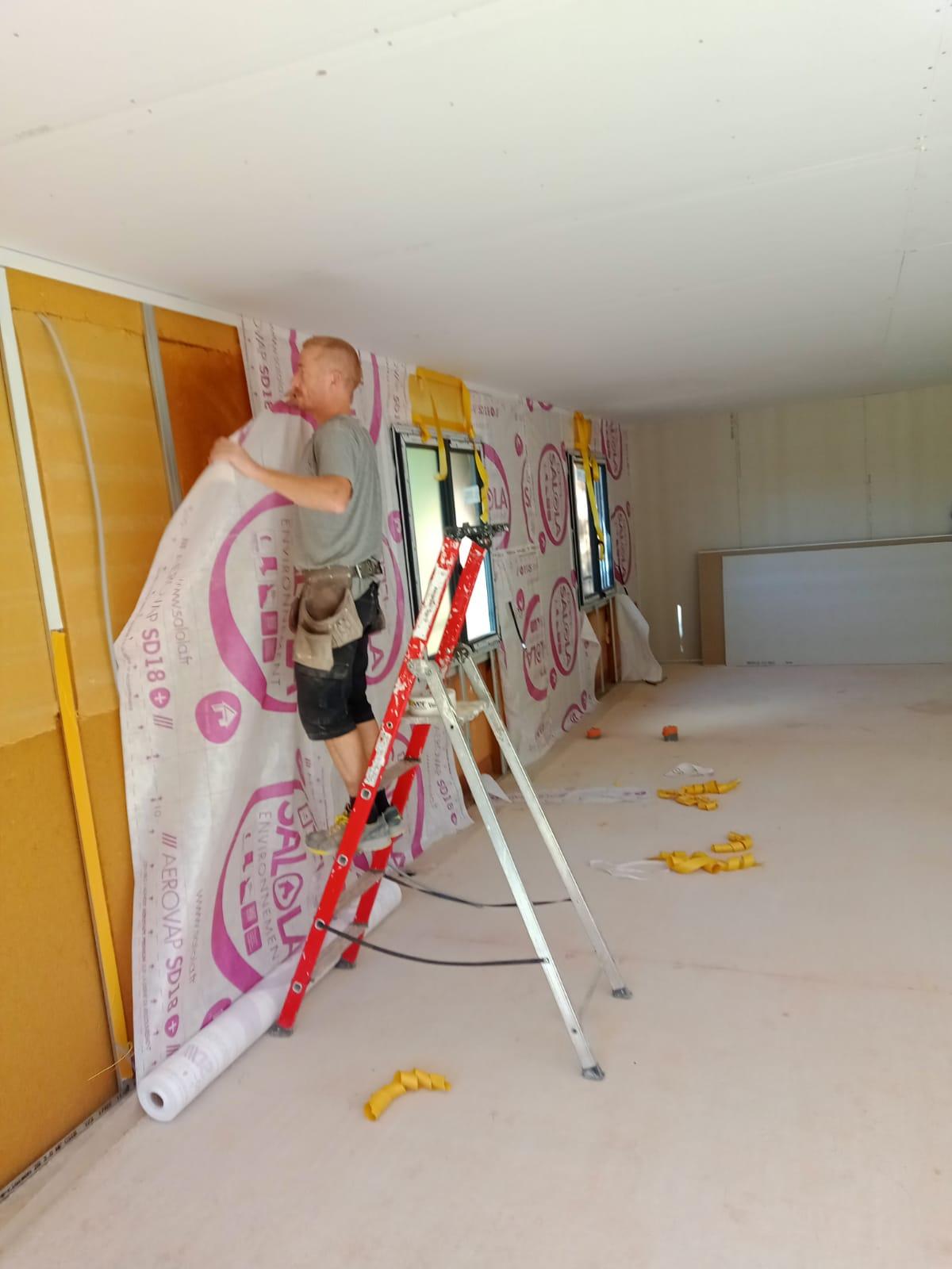 Pose d'une membrane sur une isolation murale en cours de chantier