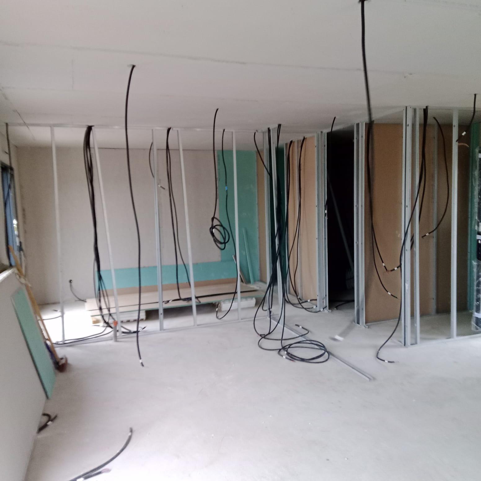 Cloisons en plaques de plâtre avec ossature métallique et câbles visibles dans une pièce en chantier.
