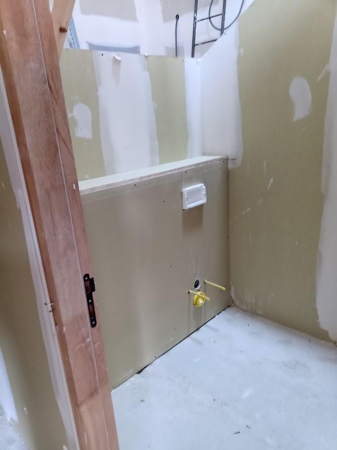 Cloison en plaques de plâtre avec raccordements de plomberie apparents dans une pièce en cours de travaux.
