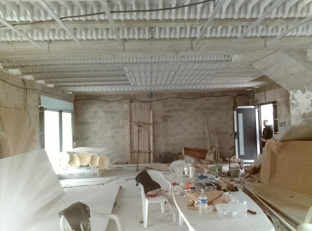 Piece en renovation avec structure de plafond apparente, rouleaux d'isolant et materiaux de chantier au sol.
