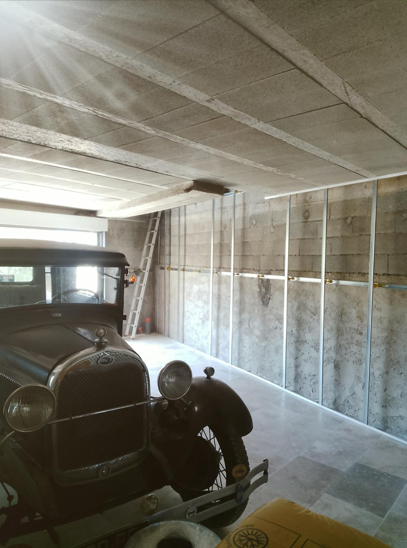 Une ossature métallique est installée devant un mur maçonné, avec un véhicule ancien visible au premier plan.