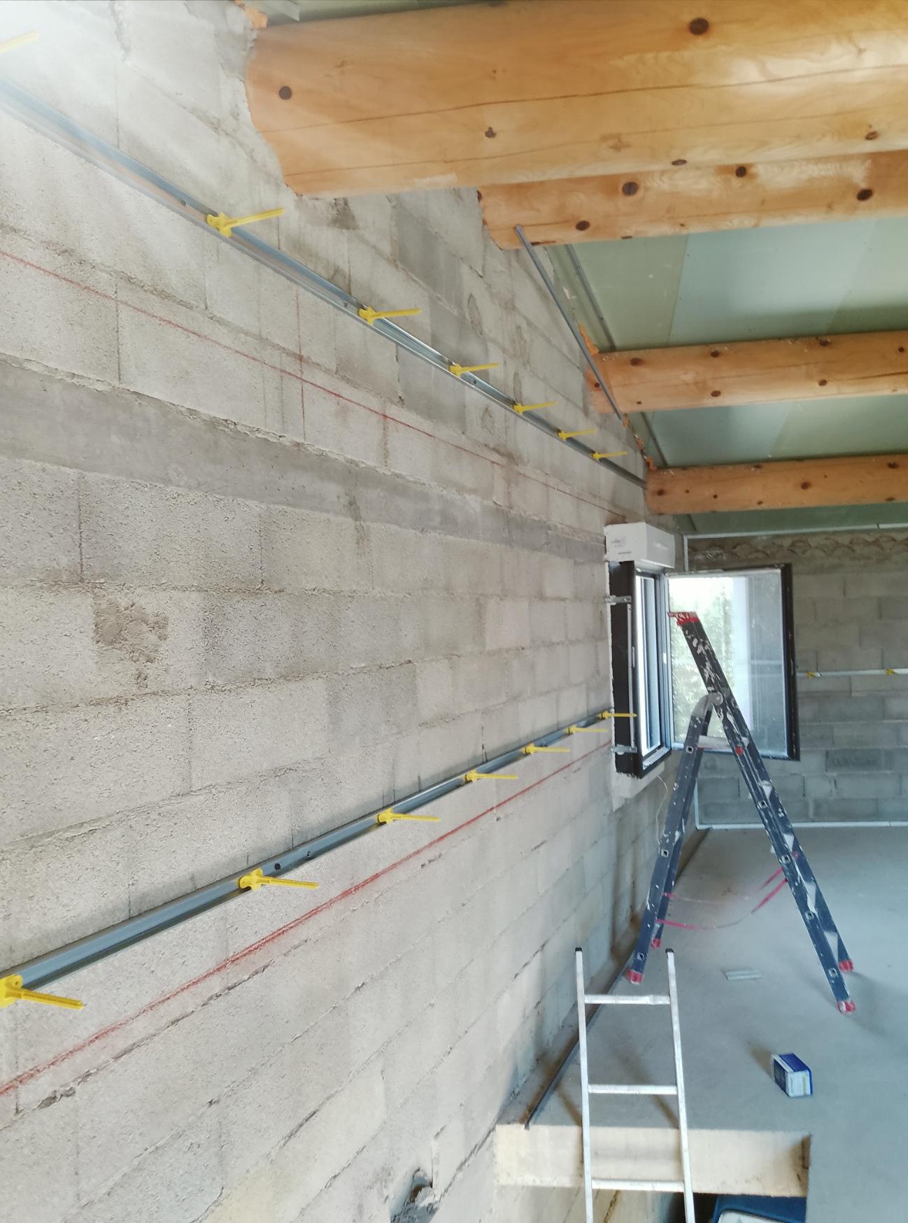 Rails métalliques fixés sur un mur en parpaings pour préparer un doublage intérieur.