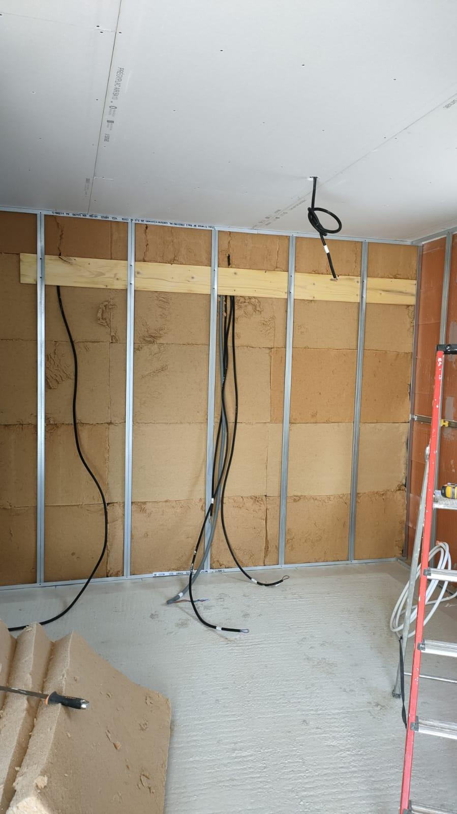 Mur en cours de réalisation avec montants métalliques, panneaux isolants visibles et câbles électriques apparents.