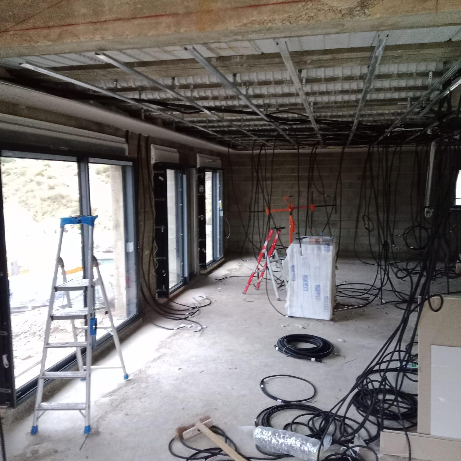 Pièce en chantier avec une ossature métallique visible au plafond, des câbles apparents et des fenêtres sur le côté.