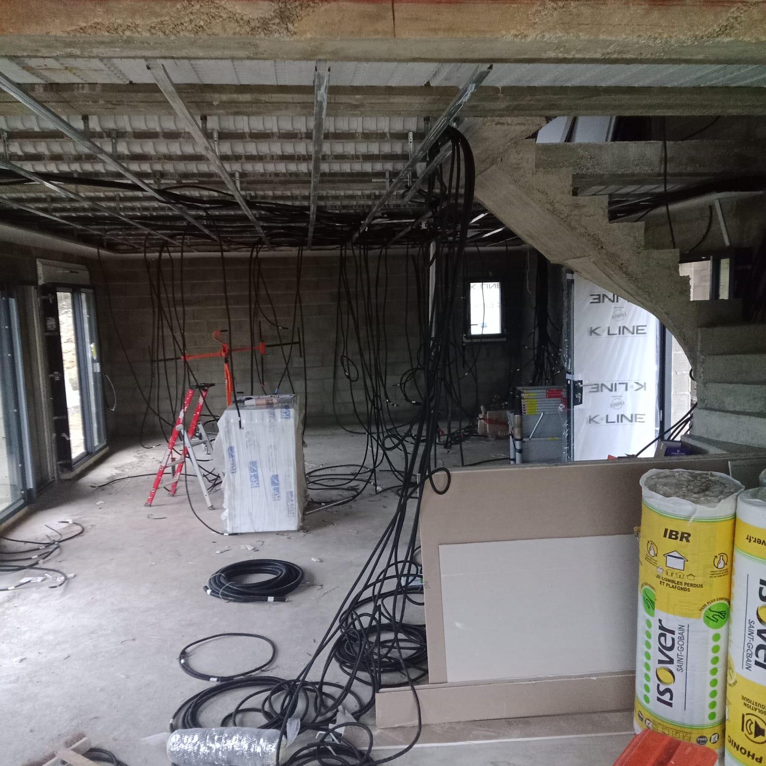 Plafond en cours de chantier avec ossature métallique, isolation apparente et câbles électriques.