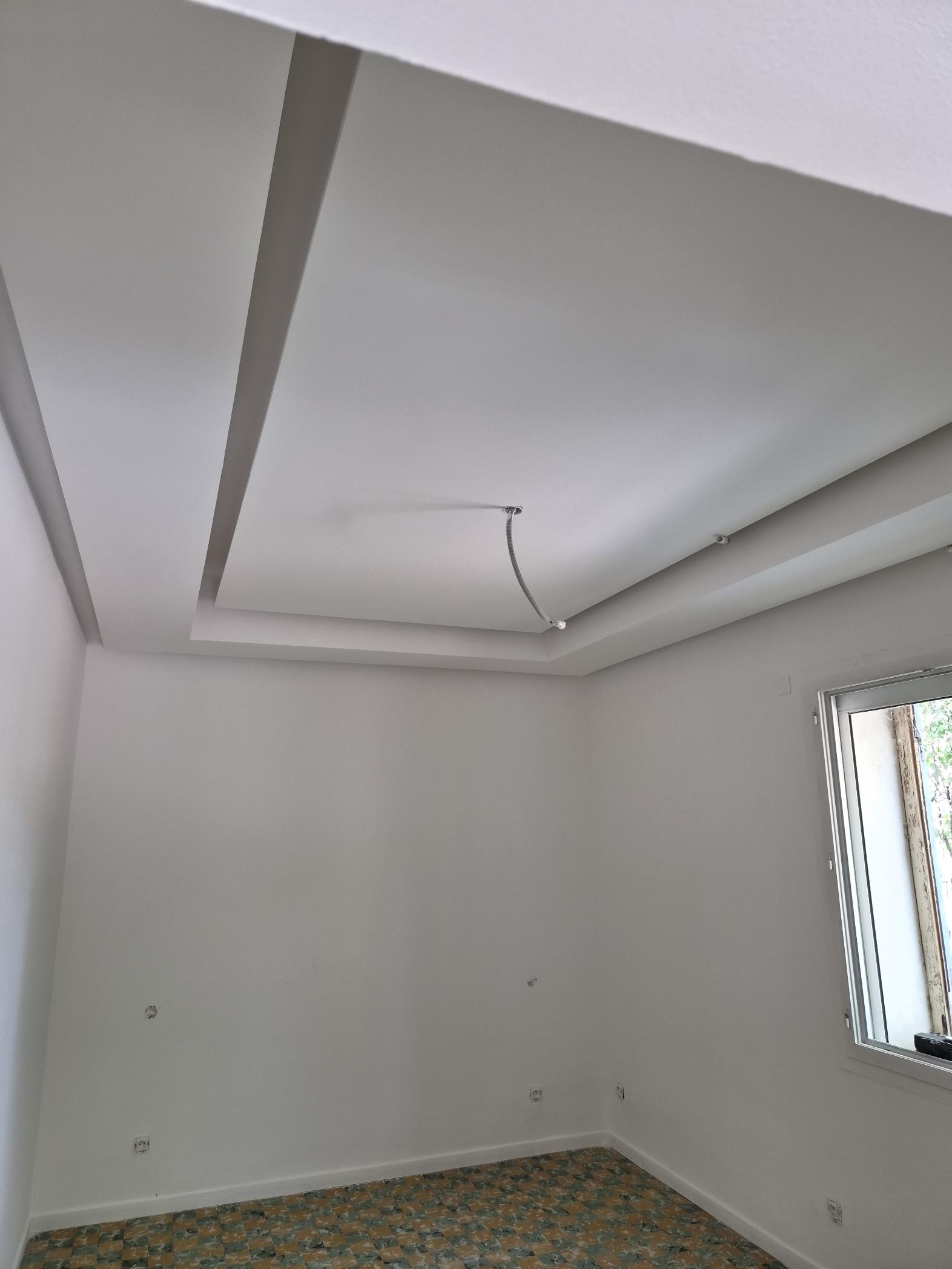 Plafond à plusieurs niveaux avec une gaine ou un câble apparent au centre de la pièce.
