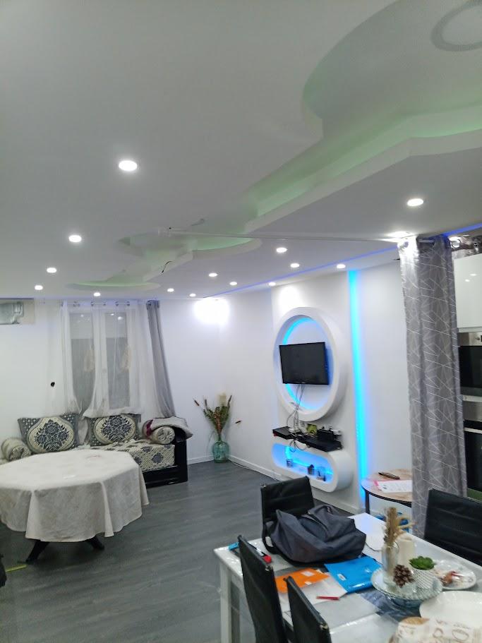 Pièce intérieure avec plafond décoratif éclairé, télévision murale et éléments muraux arrondis.