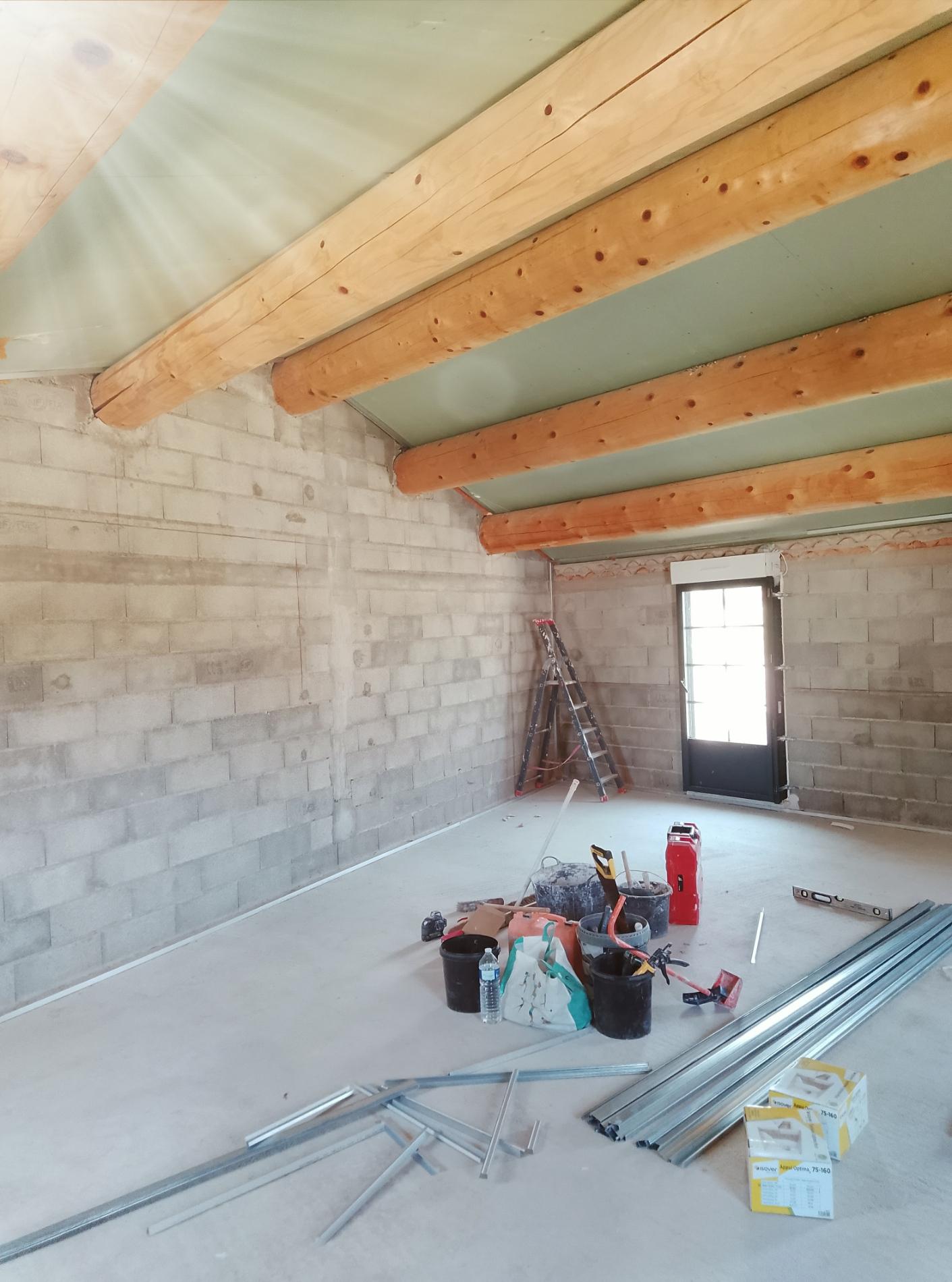 Plafond avec panneaux posés entre des poutres en bois dans une pièce en chantier.