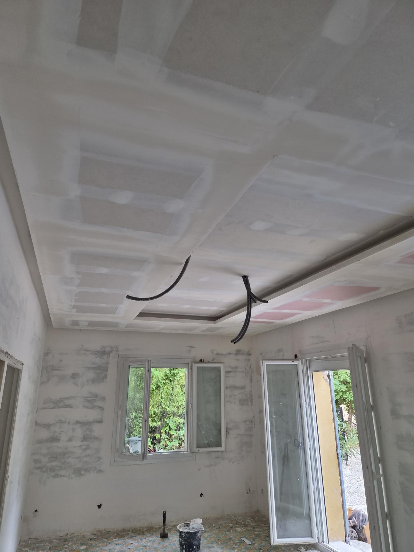 Plafond en plaques de plâtre avec joints enduits et gaines électriques apparentes dans une pièce en rénovation.