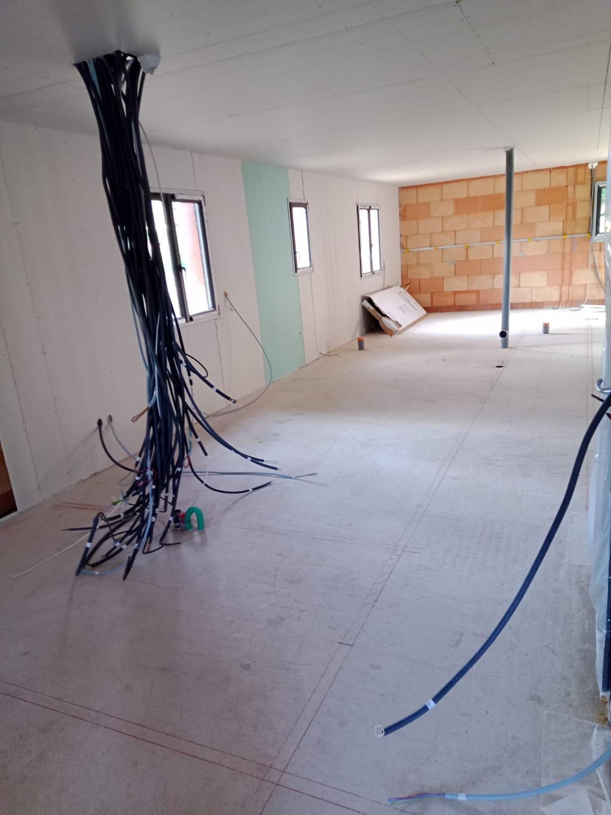 Pièce en cours d’aménagement avec murs et plafond en plaques de plâtre, câbles apparents et mur en briques visible.