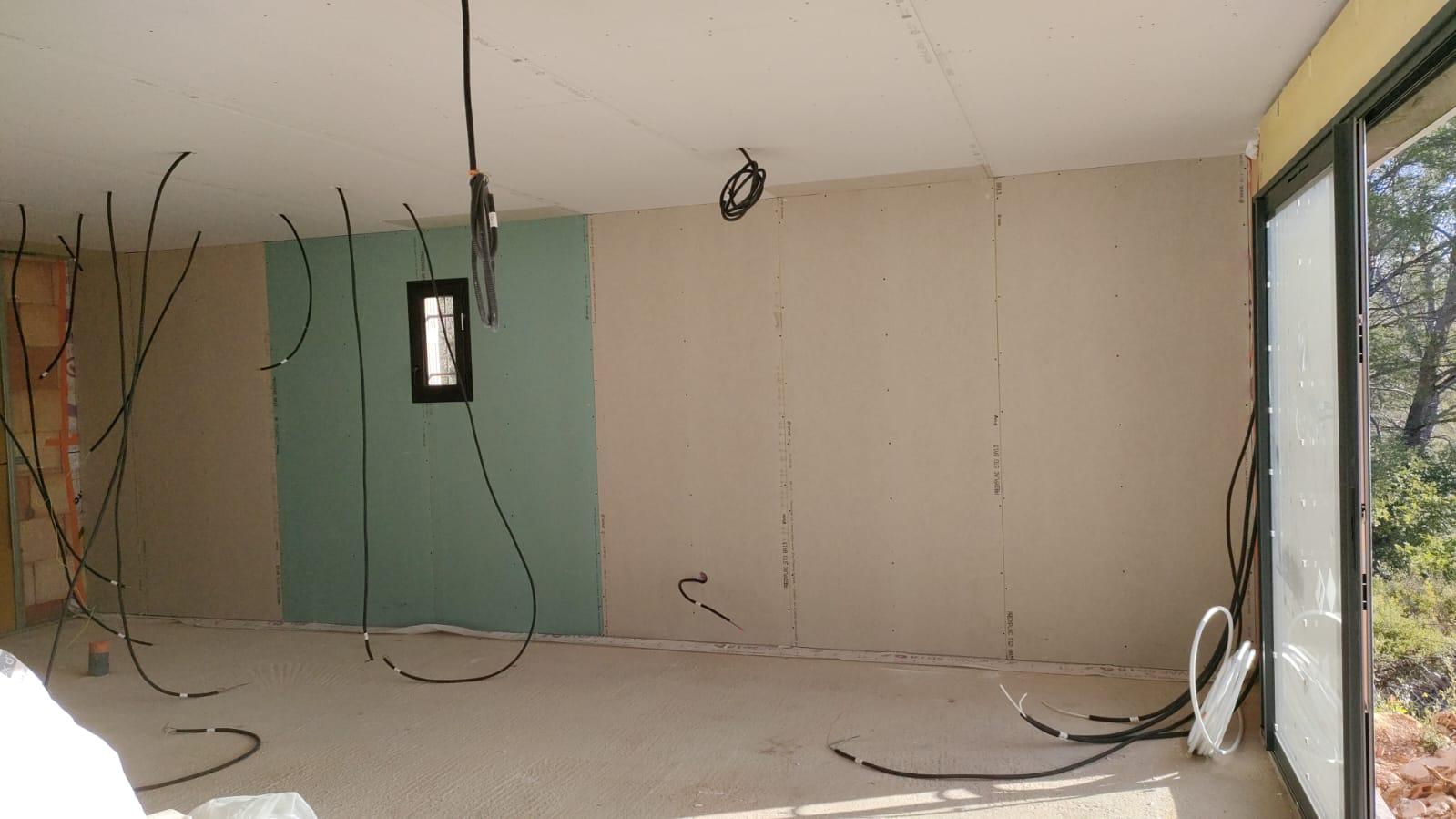 Pièce en cours d’aménagement avec des plaques de plâtre posées aux murs et au plafond, et des câbles apparents.