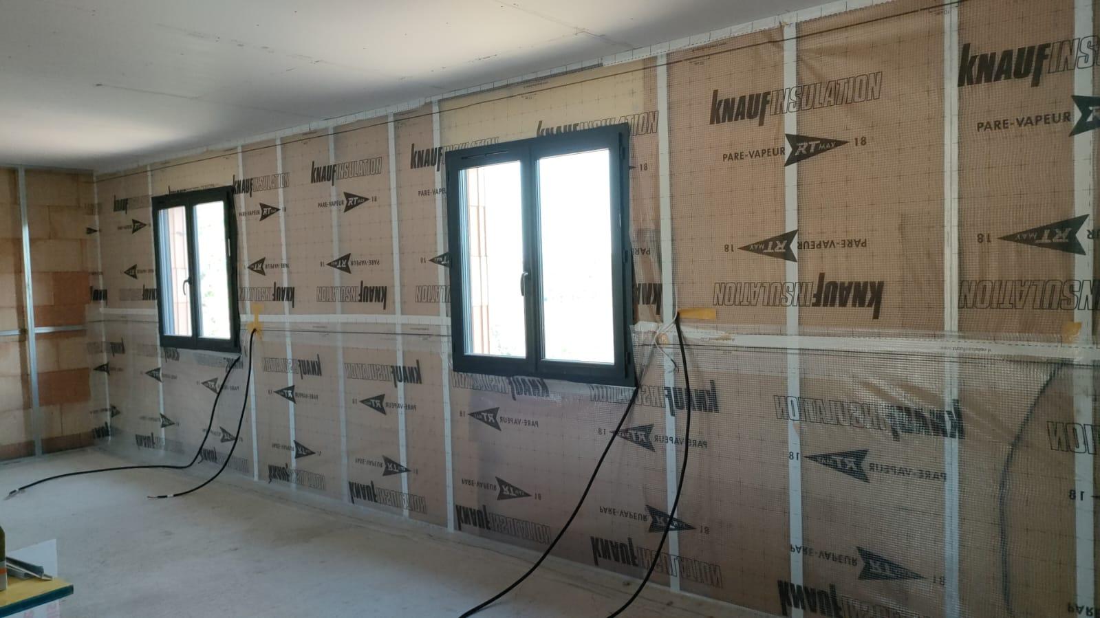 Panneaux isolants avec pare-vapeur visibles sur les murs d'une pièce en cours de chantier.