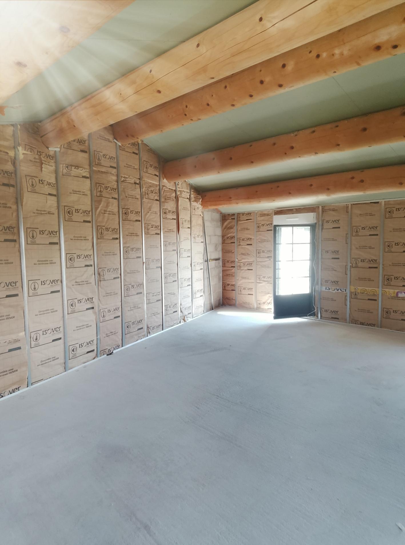 Pièces en cours d'isolation avec des panneaux visibles sur les murs et entre les poutres du plafond.