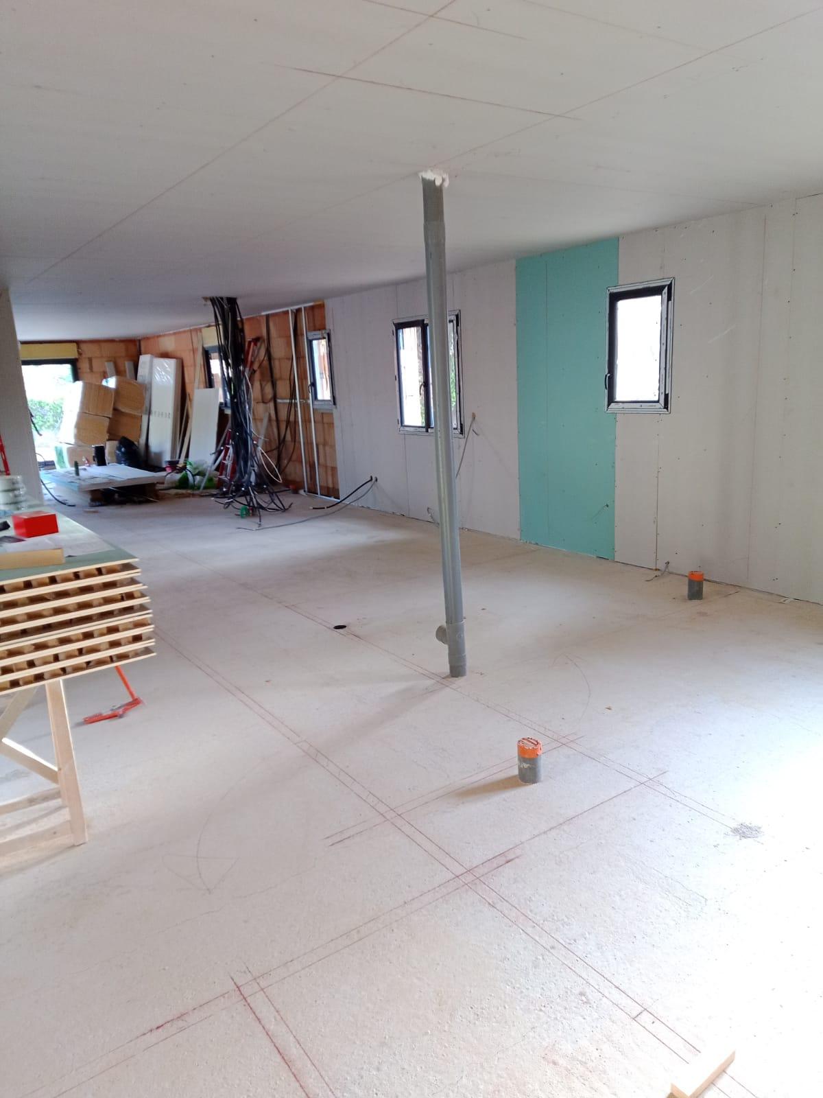 Pièce en cours d’aménagement avec plaques de plâtre posées sur les murs et au plafond, câbles et conduits encore visibles.
